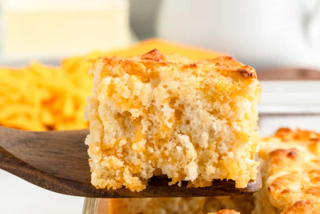 A single Cheddar Butter Swim Biscuit being lifted from the pan with a spatula, showing cheesy layers.
