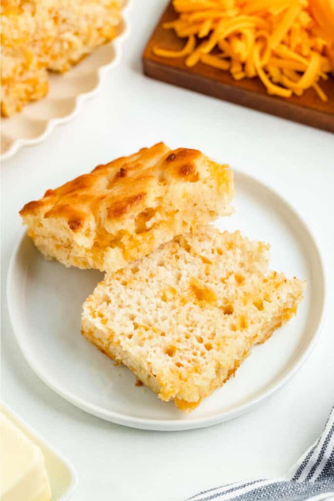 Biscuit sliced in half on a plate, revealing fluffy texture and melted cheddar inside.