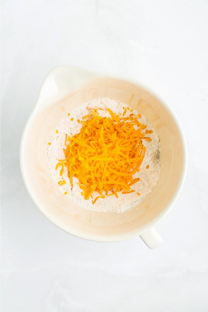 Shredded cheddar cheese added to the dry flour mixture in a large mixing bowl.