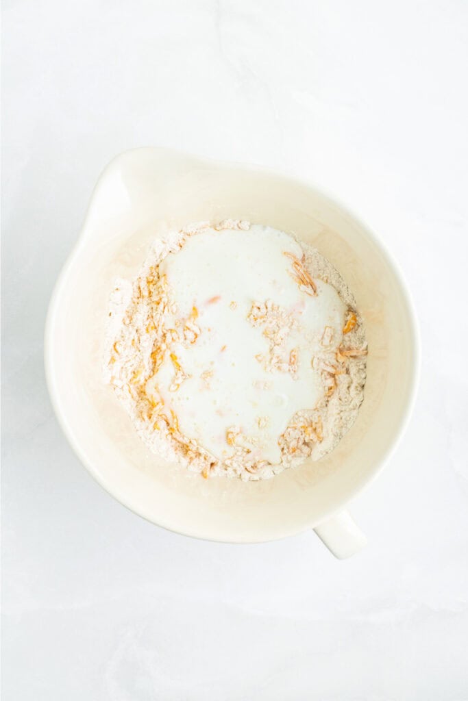 Buttermilk poured into the bowl of flour and cheddar mixture to form biscuit dough.