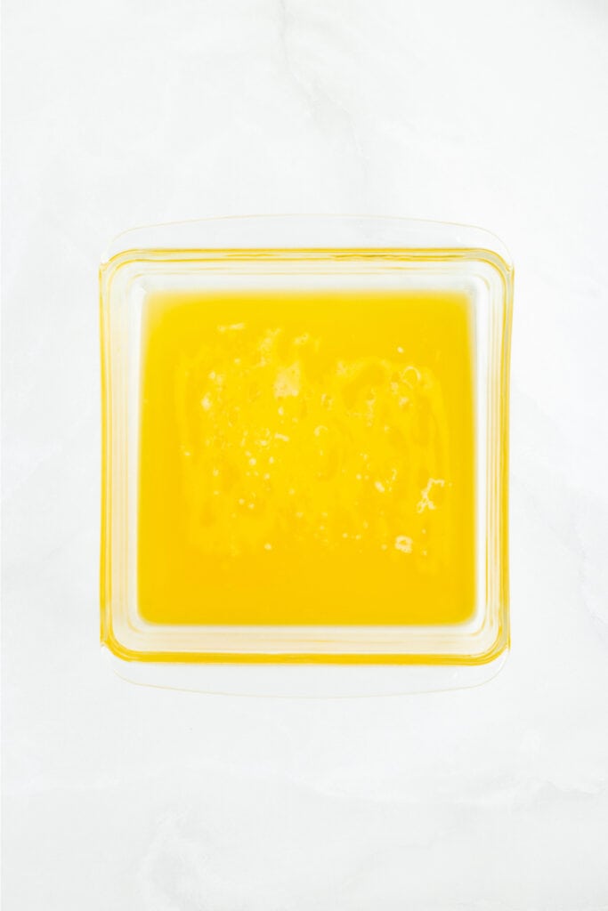 Square baking dish filled with melted butter, ready for biscuit dough.