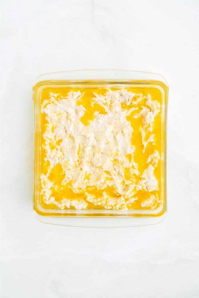 Biscuit dough spread into melted butter in a square baking dish.