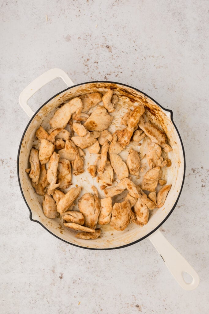 Cooked sliced chicken breast browning in a white skillet