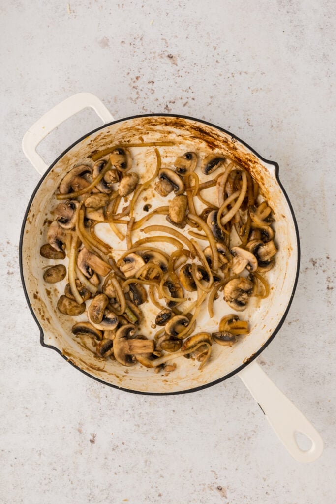 Onions and mushrooms sautéing in a white skillet