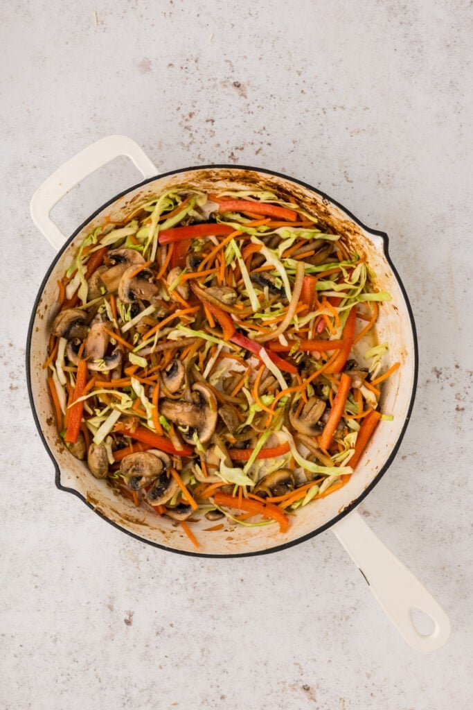Mushrooms, onions, carrots, cabbage, and red bell pepper cooking together in a skillet