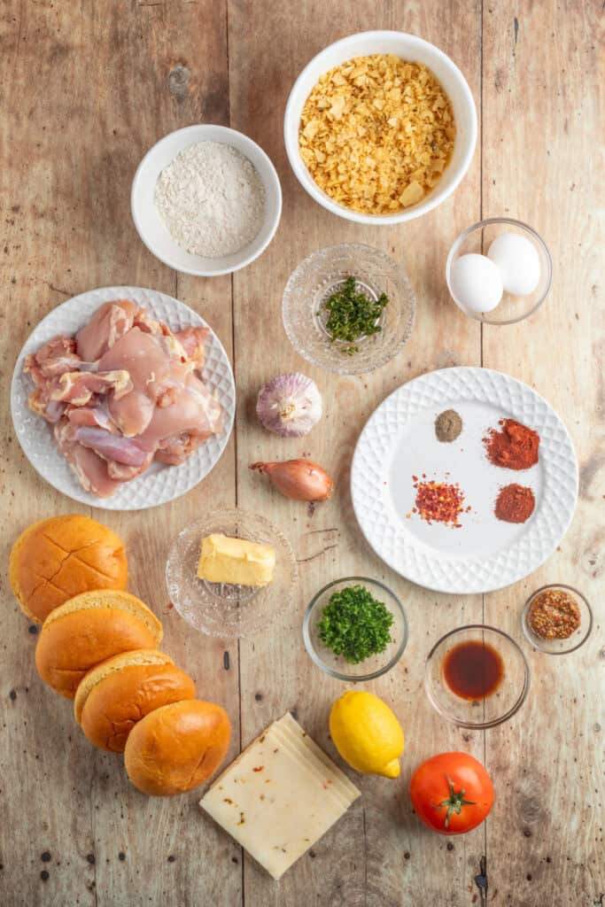 Overhead view of Cowboy Butter Crispy Chicken Sandwich ingredients including chicken thighs, buns, potato chips, flour, eggs, spices, and herbs laid out on a rustic wooden table