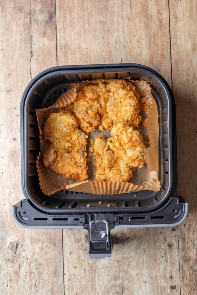 Crispy potato chip-coated chicken thighs air frying in a basket lined with parchment paper.