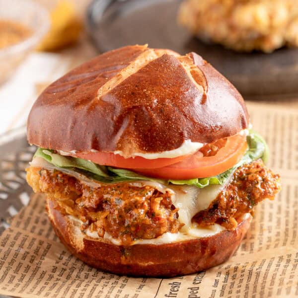 Square image of Cowboy Butter Crispy Chicken Sandwich on a pretzel bun with tomato, lettuce, and cheesy cowboy butter chicken.