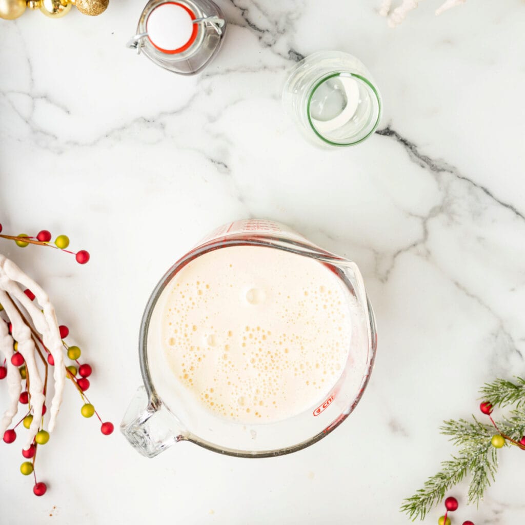 Freshly strained eggnog base in a glass measuring cup with bubbles on the surface.