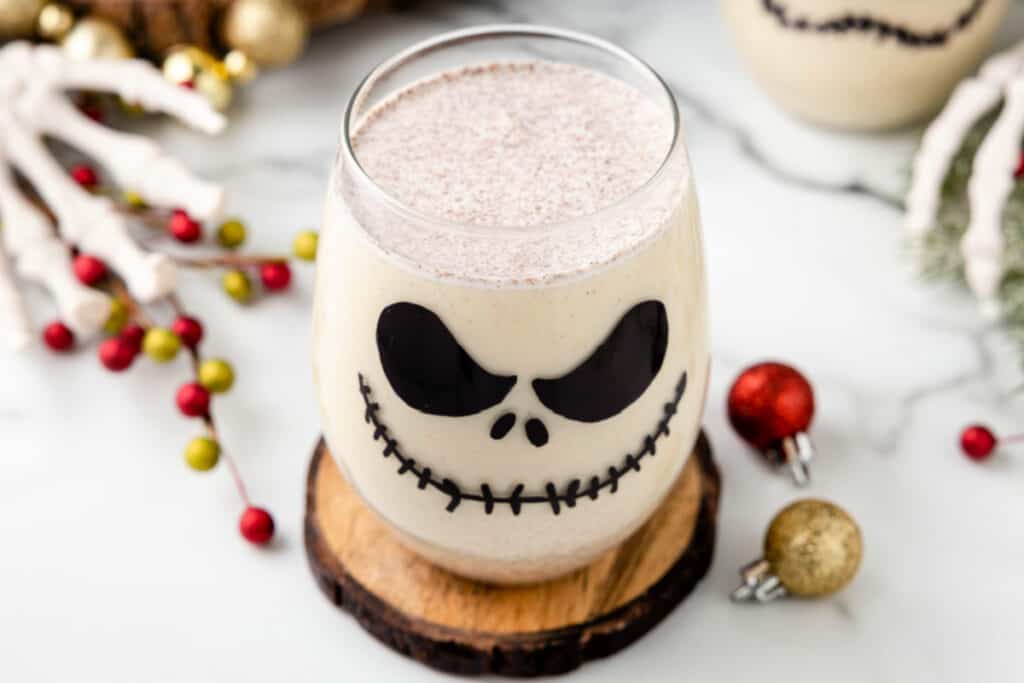 Wide shot of a Jack Skellington Cocktail served in a themed glass on a wooden coaster, with festive decor around.