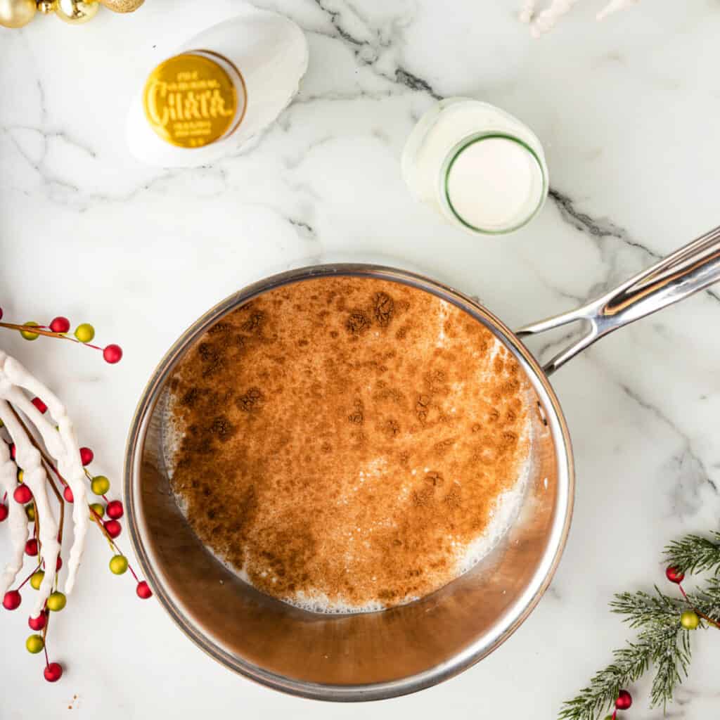 Pumpkin spice sprinkled into a saucepan of warm milk, beginning to simmer with festive decorations around the pan.