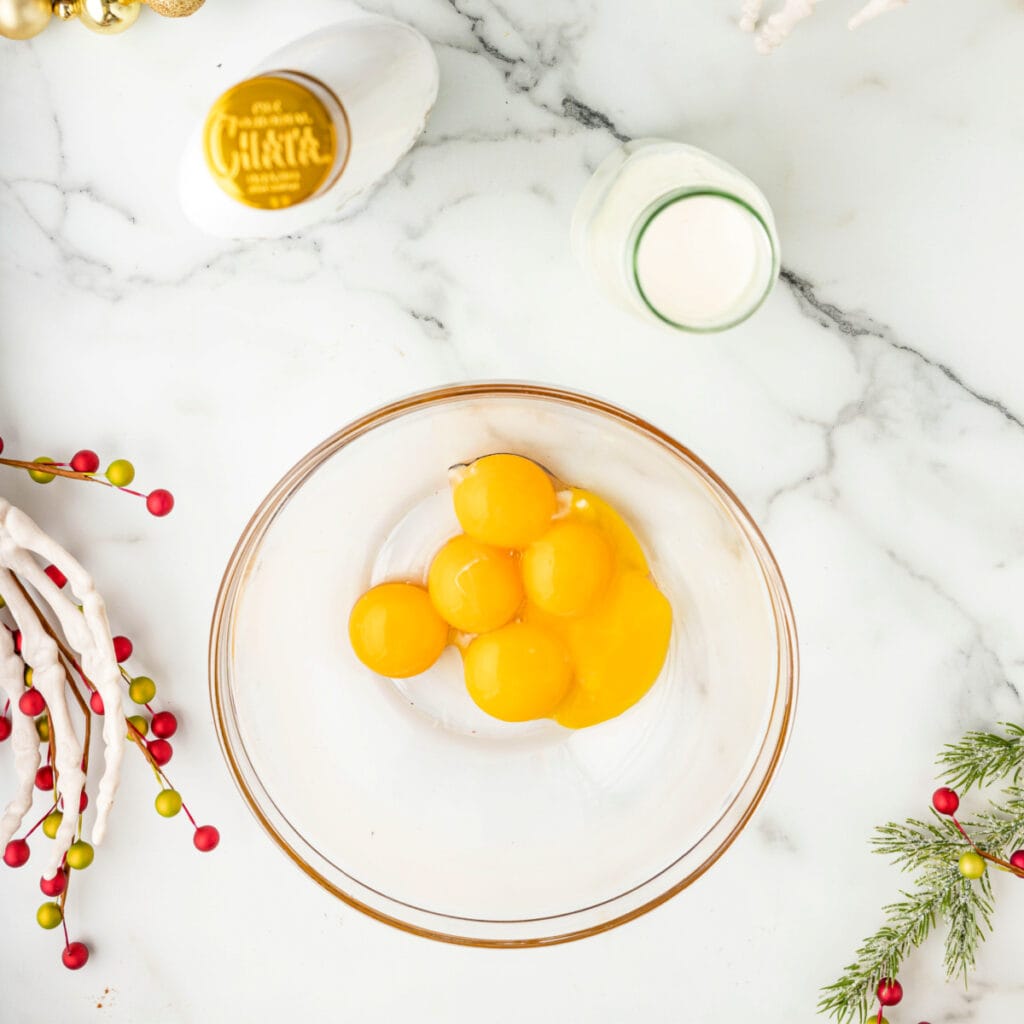 Bowl with raw egg yolks set on a marble counter next to cream and RumChata.