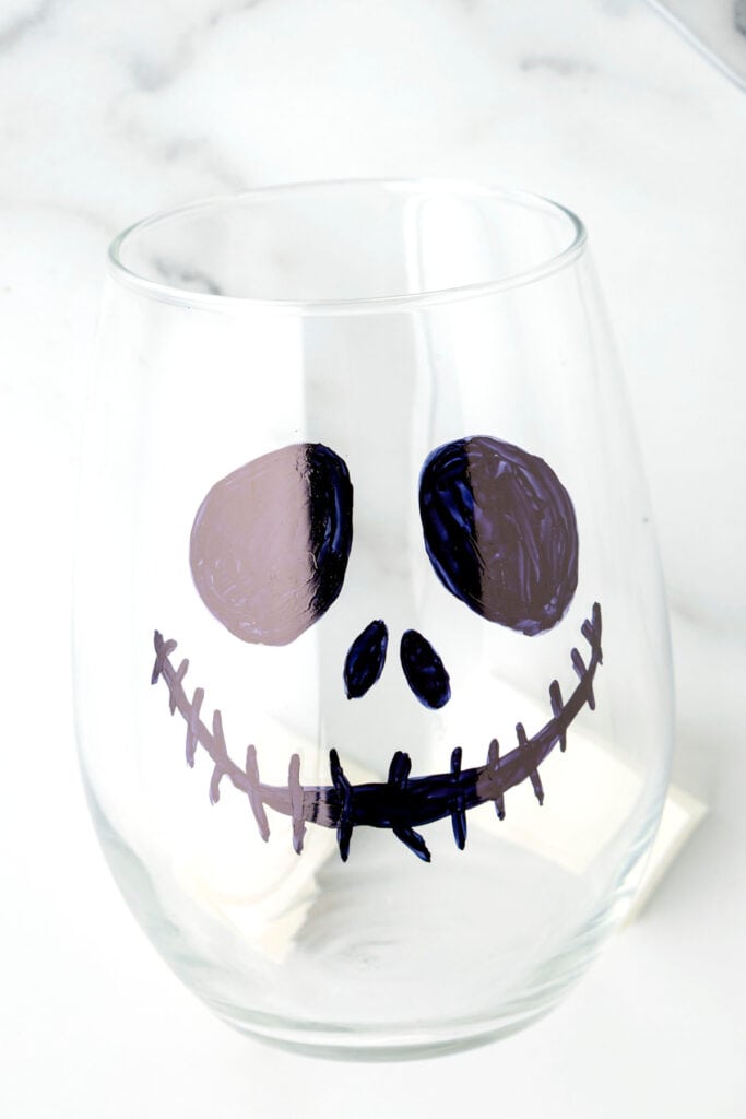 A finished traced Jack Skellington face on a clear glass with bold black eyes, nose, and stitched smile.