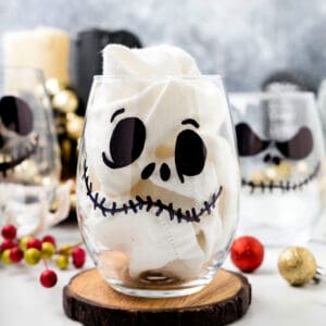 Square image of a Jack Skellington glass with a napkin inside, surrounded by festive holiday decorations.