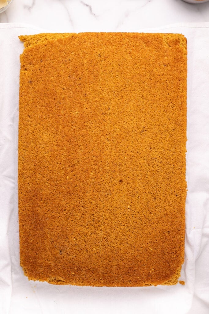 Baked pumpkin roll cake laid flat on a sugared towel, ready to be rolled.