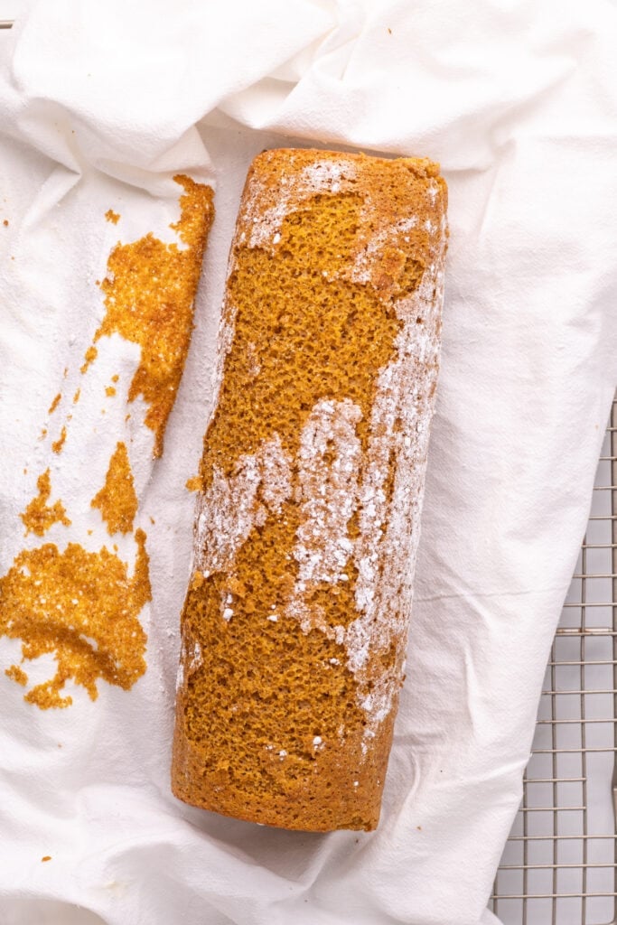 Rolled pumpkin cake dusted with powdered sugar on a towel.
