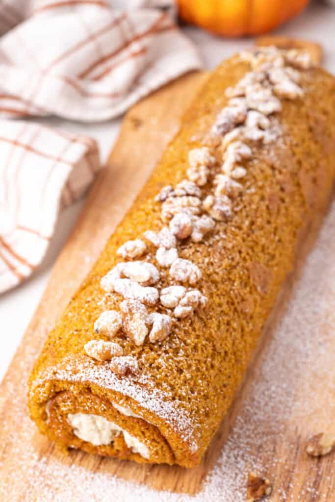 Finished pumpkin roll decorated with powdered sugar and walnuts on a wooden board.