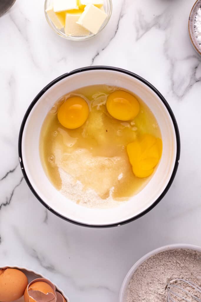 Large bowl with eggs and sugar before mixing, butter cubes visible in the background.