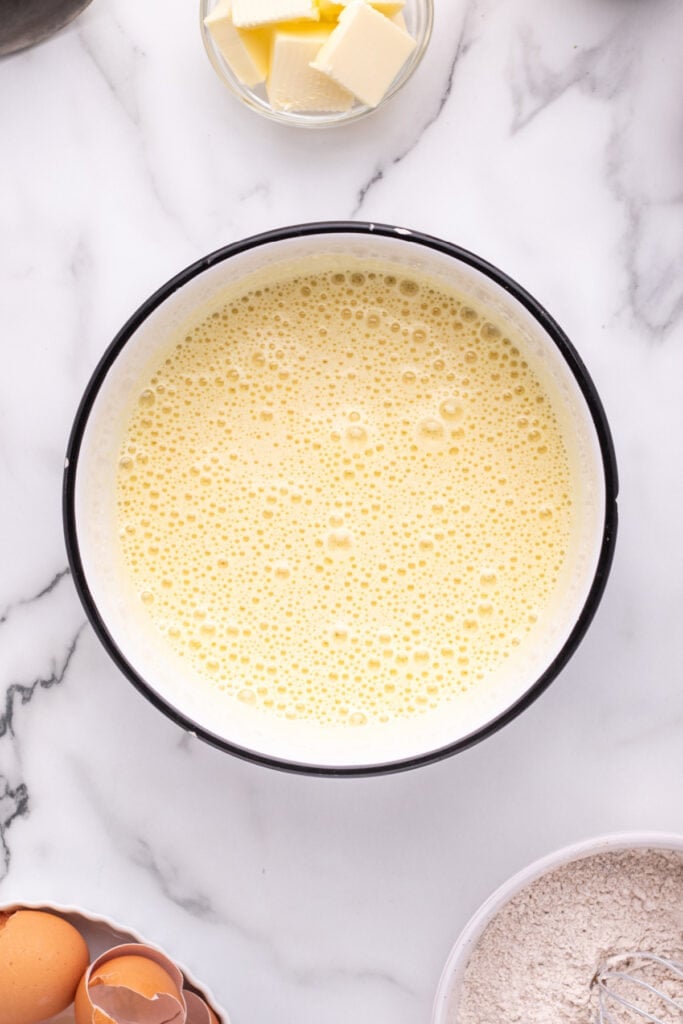 Beaten eggs and sugar mixture in a white bowl, light and frothy.