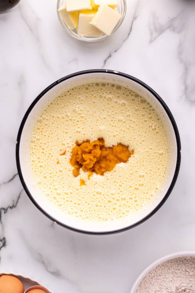 Pumpkin puree added to the egg and sugar mixture in a mixing bowl.