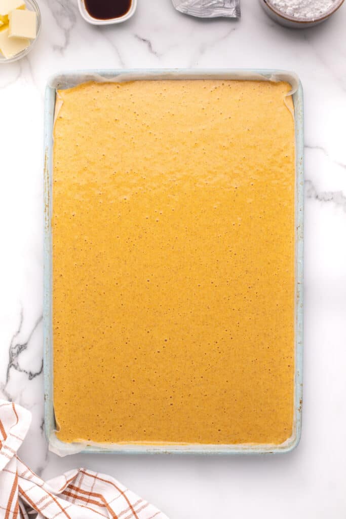 Pumpkin roll batter spread evenly in a parchment-lined jelly roll pan before baking.