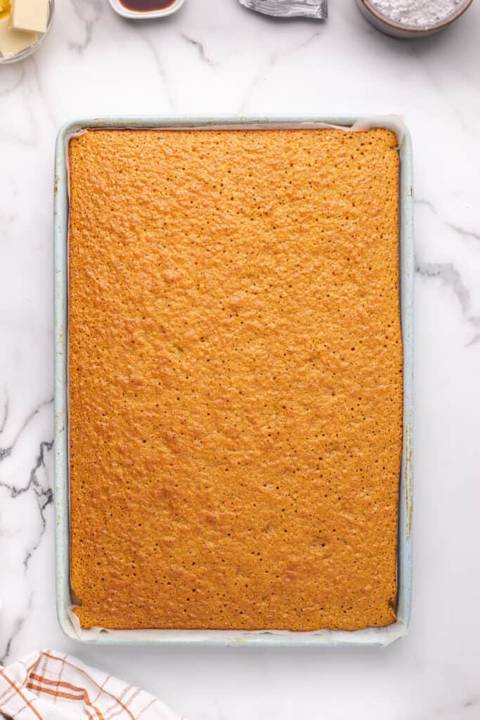 Baked pumpkin roll cake still in the jelly roll pan, golden brown and set.