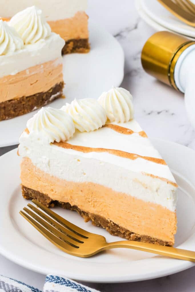 Slice of no bake RumChata pumpkin cheesecake on a white plate with a gold fork, showing creamy pumpkin and RumChata layers.
