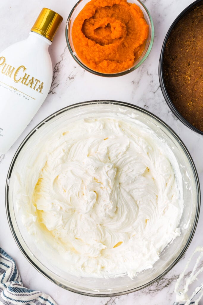 Smooth and fluffy cheesecake base mixture after folding in cool whip, with pumpkin puree and RumChata nearby.