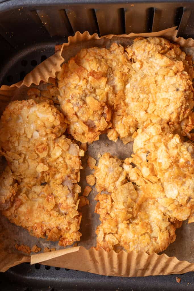 Four breaded chicken thighs with a crunchy potato chip coating inside an air fryer basket lined with parchment paper.