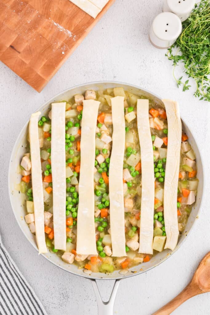 Skillet filled with turkey pot pie mixture topped with vertical puff pastry strips.