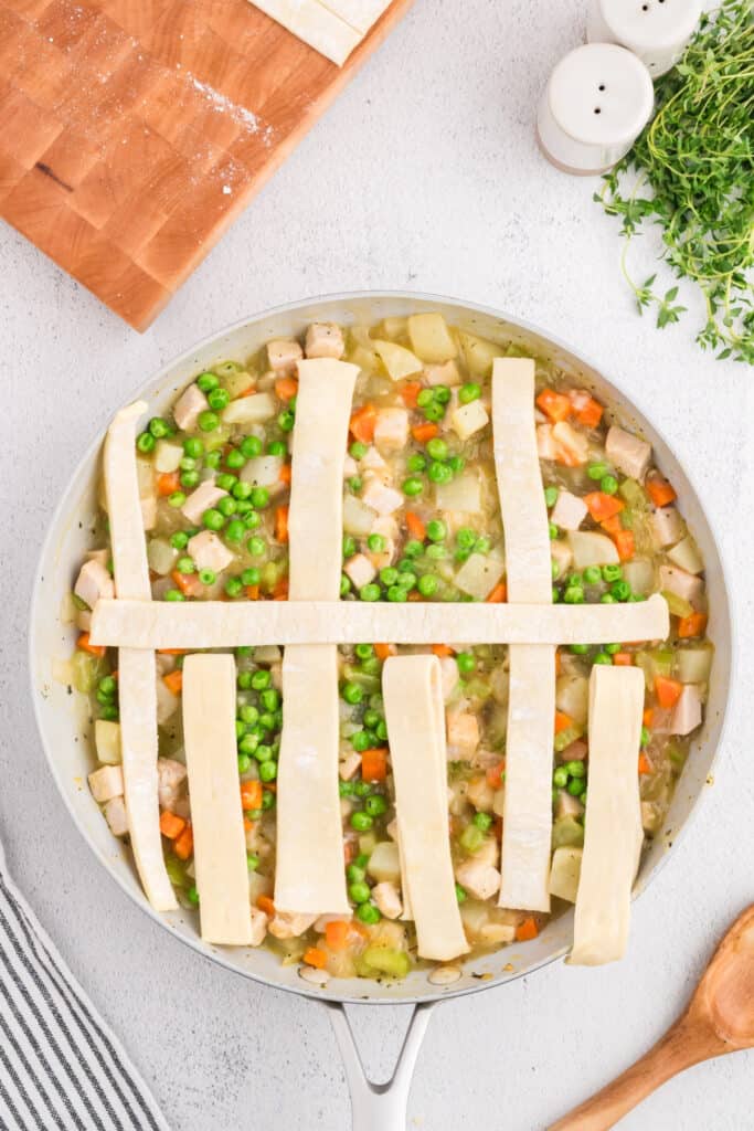 Puff pastry strips being woven into a lattice pattern over turkey pot pie filling.