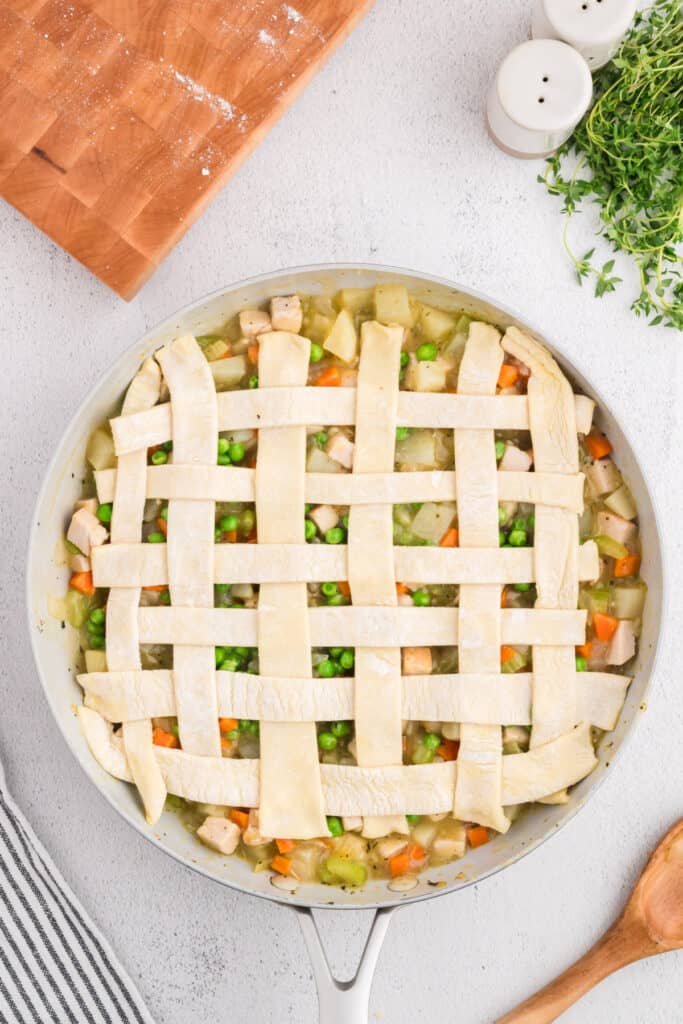 Nearly completed puff pastry lattice topping over turkey pot pie mixture in skillet.