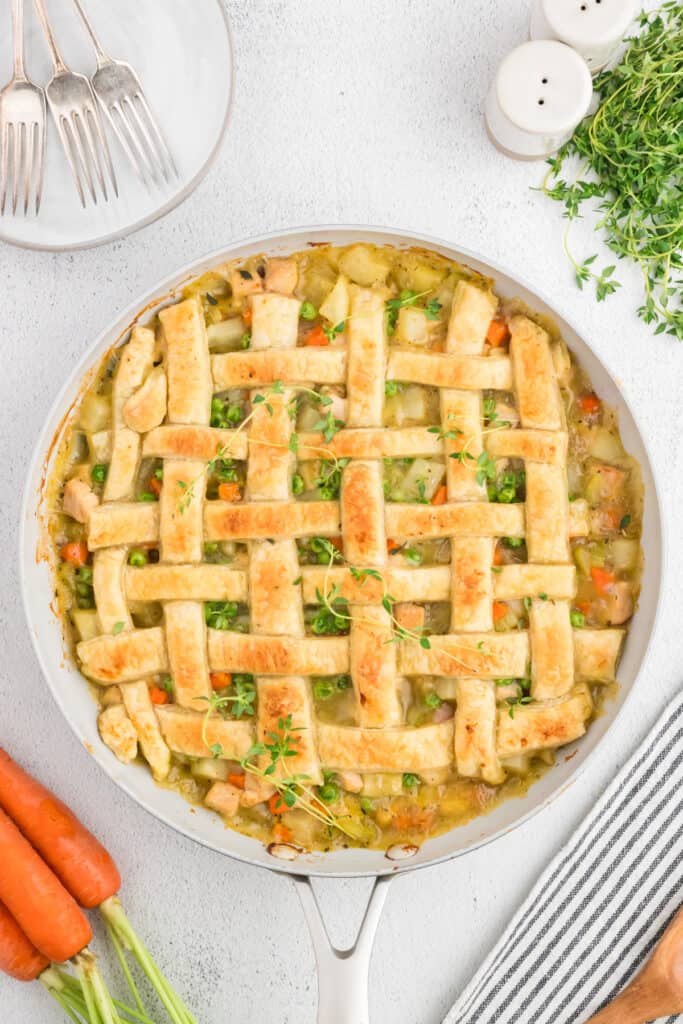 Baked puff pastry turkey pot pie in skillet, golden brown lattice crust with fresh thyme.