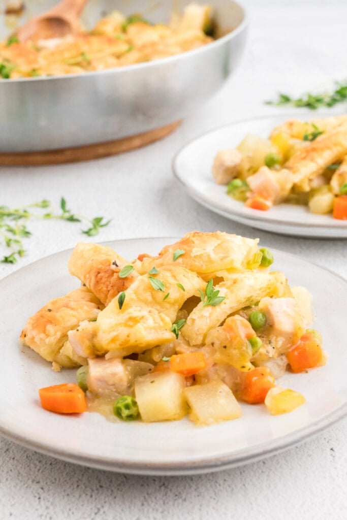 Plate of puff pastry turkey pot pie served with golden crust, peas, carrots, and potatoes.