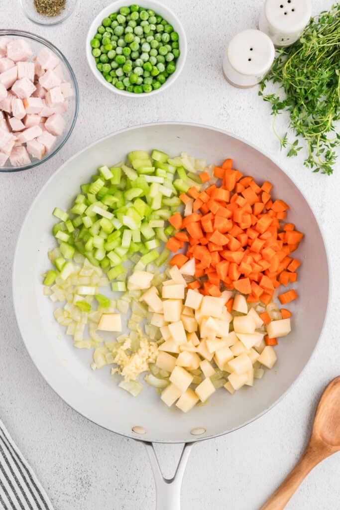 Carrots, celery, potatoes, and garlic added to sautéed onions in skillet, with peas and turkey set aside.