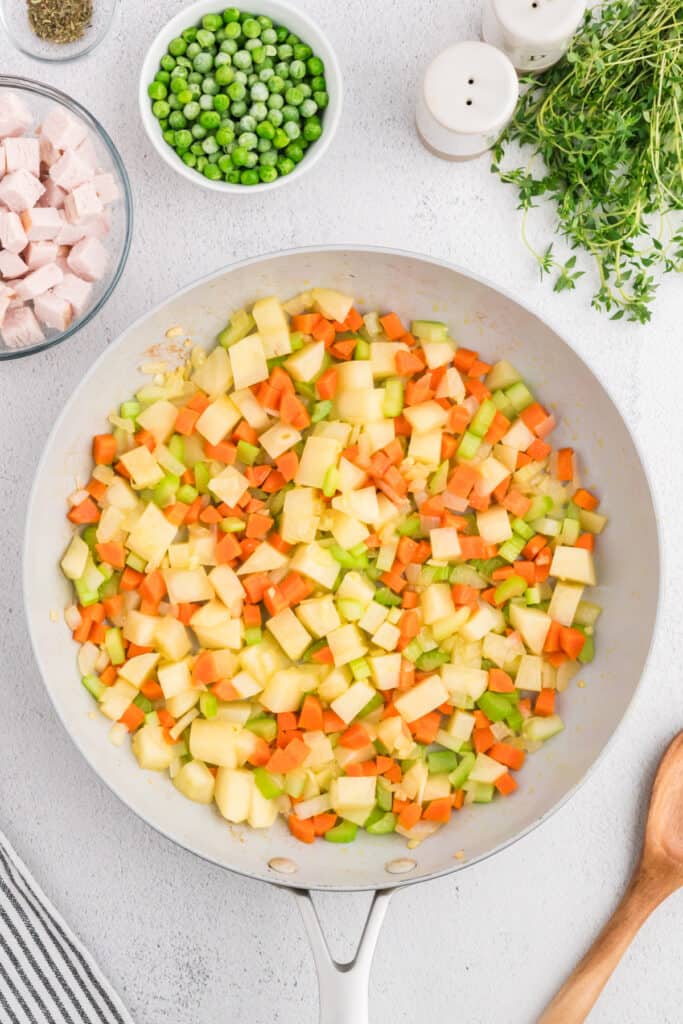 Mixed carrots, celery, and potatoes cooking together in a skillet after being stirred with onions.