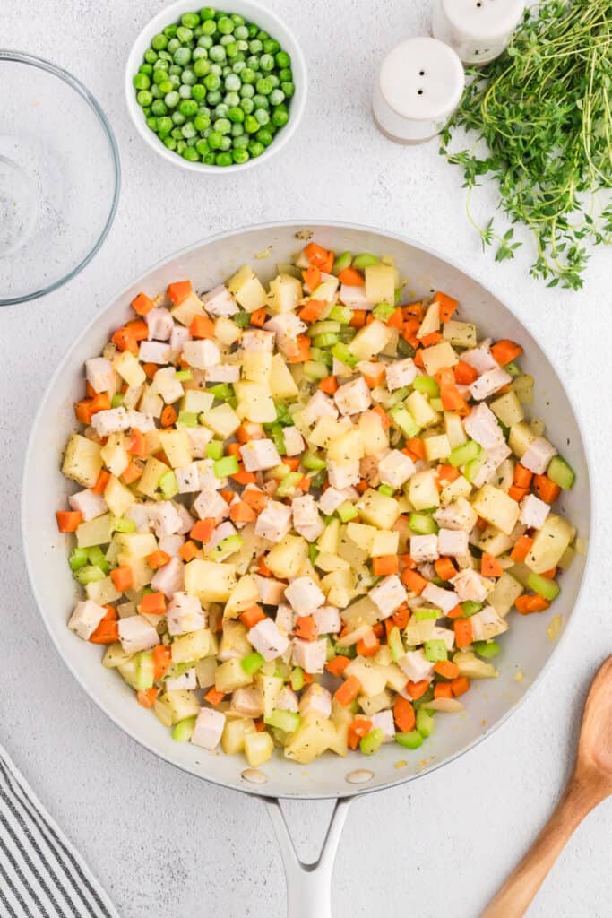 Turkey and vegetables combined in skillet, cooked down with herbs, peas waiting to be added.