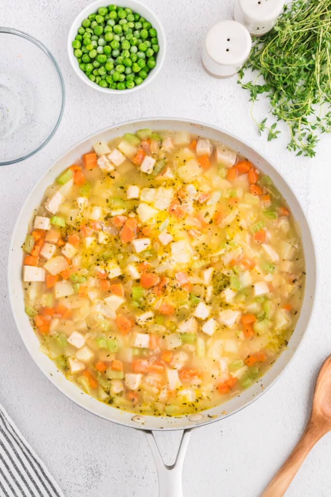 Turkey, potatoes, carrots, and celery simmering in broth in skillet, thickening into filling.