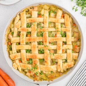 Overhead view of baked puff pastry turkey pot pie with golden lattice crust and fresh thyme garnish.