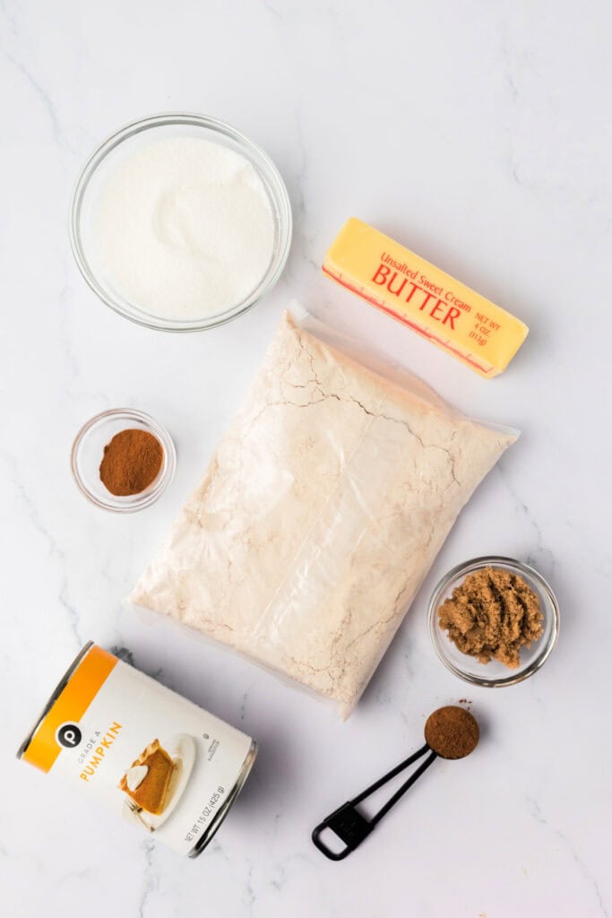 Ingredients for pumpkin donut holes including spice cake mix, canned pumpkin, butter, sugar, brown sugar, and spices on a white surface.