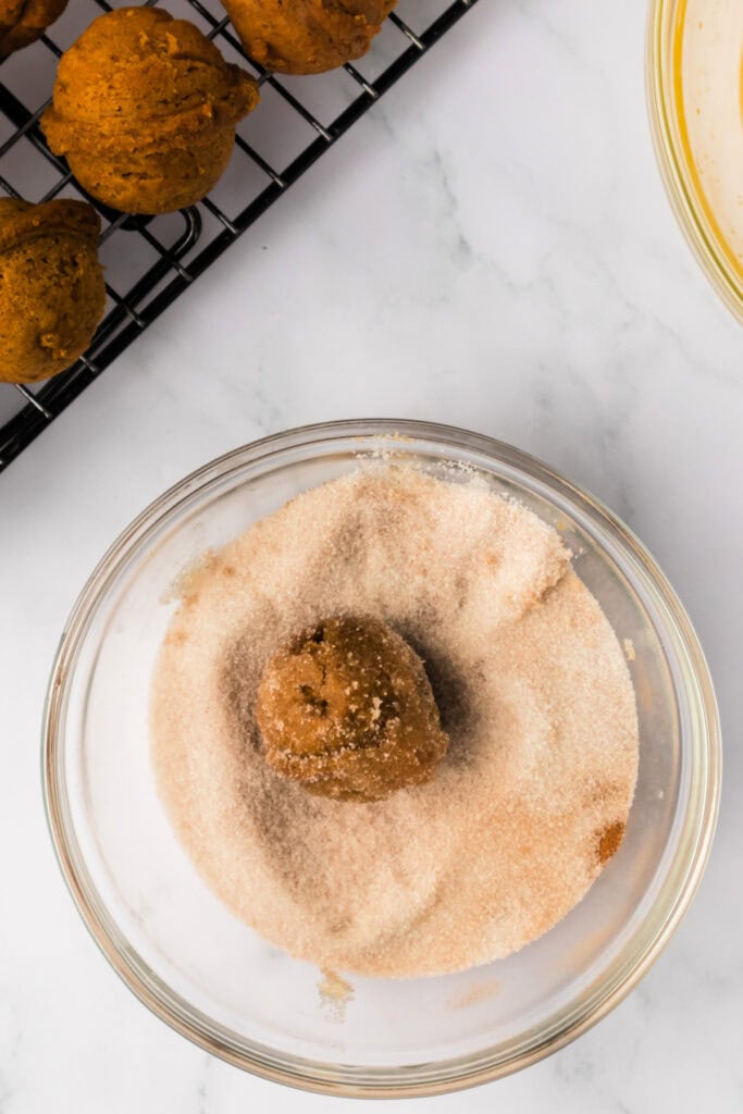 Pumpkin donut hole being rolled in cinnamon sugar mixture to finish the coating.