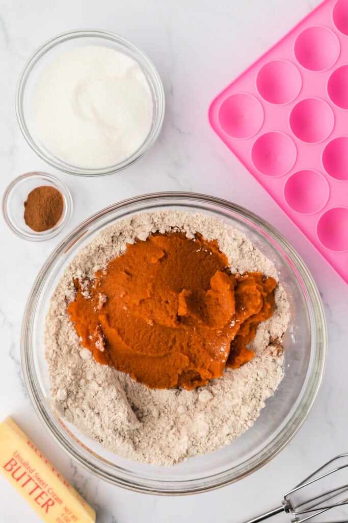 Large mixing bowl with dry ingredients and canned pumpkin puree on top, ready to be mixed for pumpkin donut holes batter.