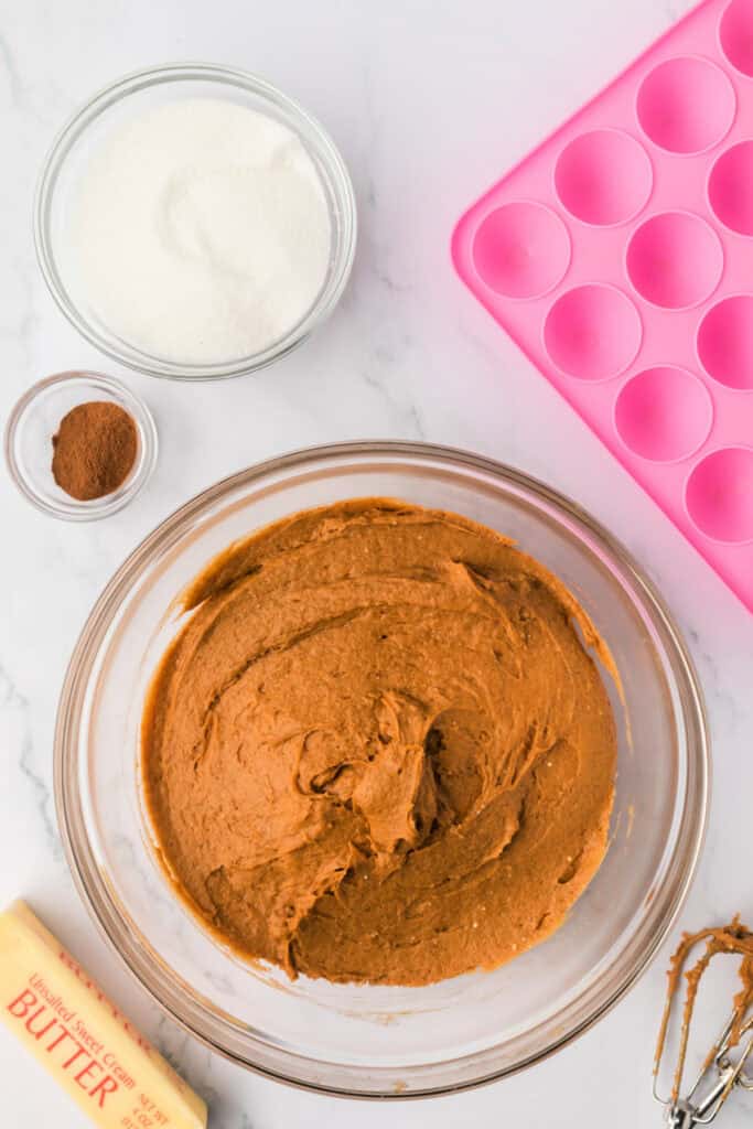Smooth pumpkin donut holes batter mixed together in a clear bowl with a pink silicone mold in the background.