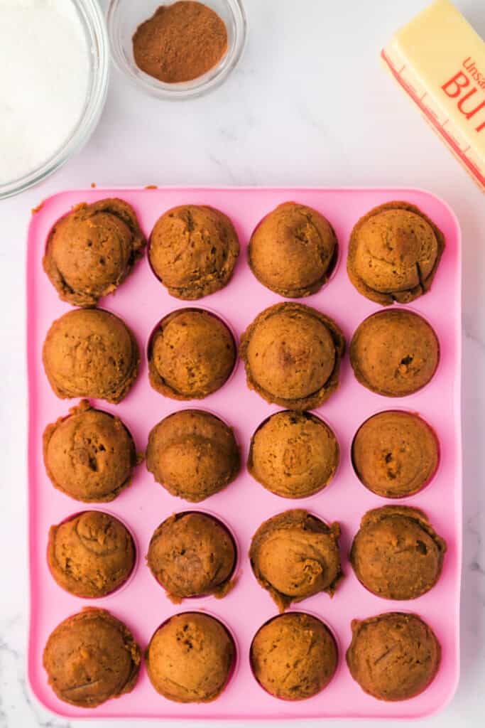 Baked pumpkin donut holes cooling in a pink silicone mold, golden brown and puffed.