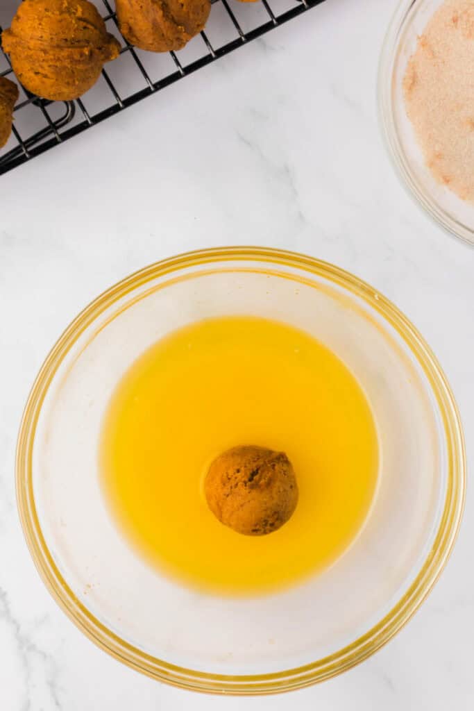 Pumpkin donut hole dipped into melted butter, ready to be coated in cinnamon sugar.