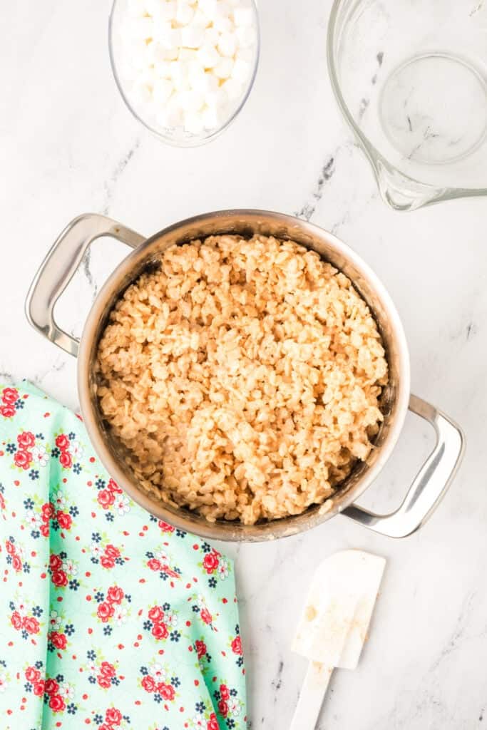 Mixture of crispy rice cereal and melted marshmallows being stirred together in a large stainless steel pot.
