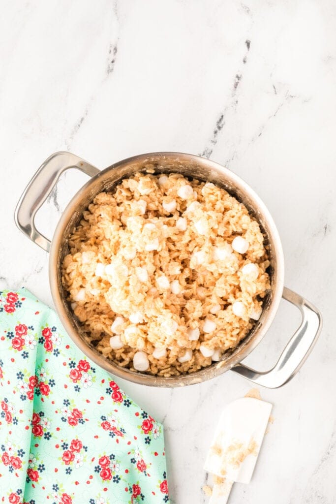 Gooey rice crispy mixture with partially melted marshmallows stirred in, creating a soft and chewy texture.