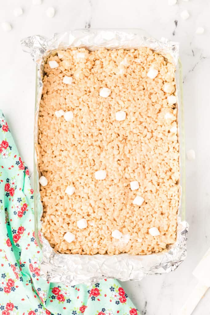 Browned Butter Rice Crispy Treats pressed into a foil-lined pan, cooling before cutting into squares.
