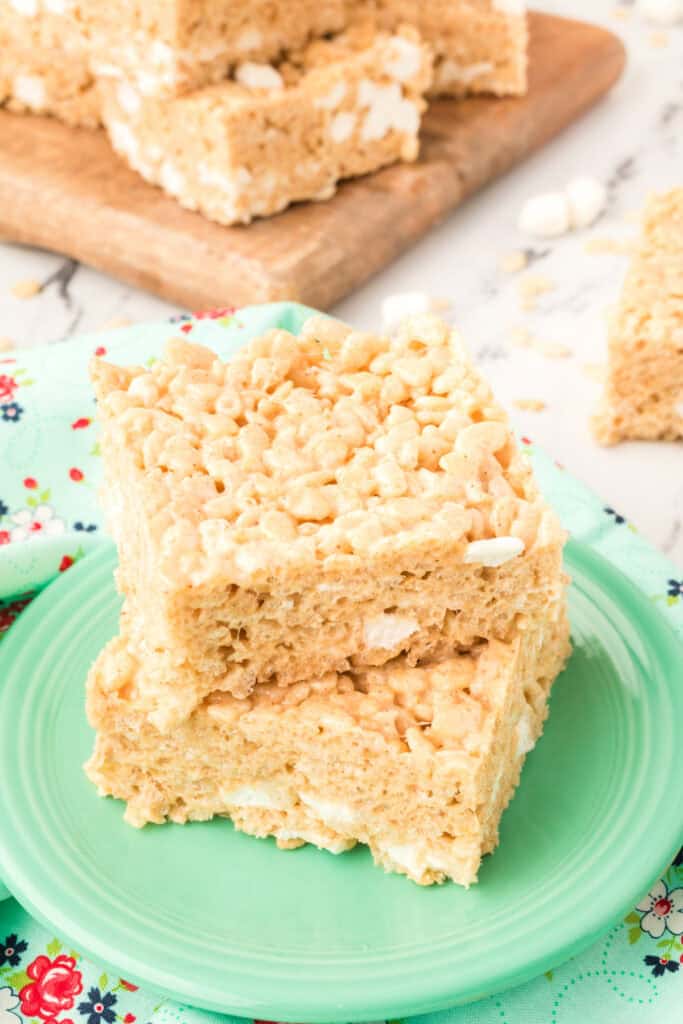 Two stacked Browned Butter Rice Crispy Treats on a green plate with more bars in the background on a wooden board.