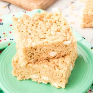 Square crop of two thick, gooey Browned Butter Rice Crispy Treats stacked on a green plate with visible marshmallow pockets.